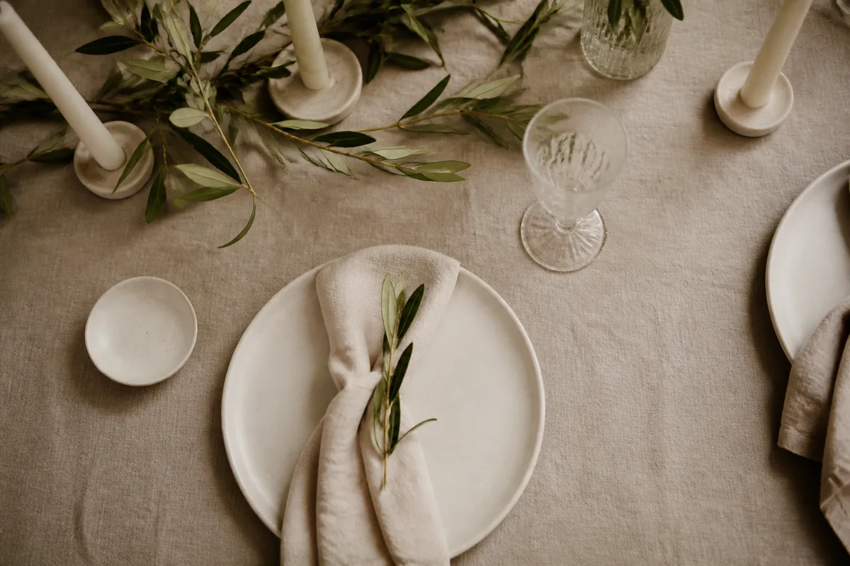 A linen reception table set with ivory plates and olive sprigs